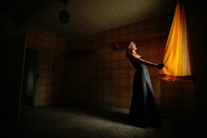 standing woman wearing black dress holding curtain 1351050 1 scaled